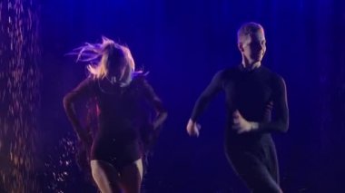 Arka planda mavi ışıkta dans eden bir çift. Genç dansçılar suyun yüzeyinde hareket eder ve birçok sıçrama yaratır. Ağır çekim. Kapat..