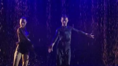 Arka planda mavi ışıkta dans eden bir çift. Genç dansçılar suyun yüzeyinde hareket eder ve birçok sıçrama yaratır. Ağır çekim. Kapat..