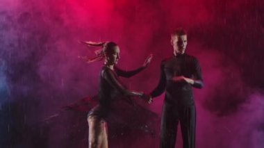 Genç çift dumanlı bir arka planda neşeli bir şekilde dans ediyor ve arka planı kıpkırmızı. Ağır çekim. Kapat..
