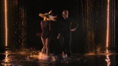 Profesyonel bir çift dansçı yağmur birikintilerinde su damlaları altında gevezelik eder. Yavaş çekim.