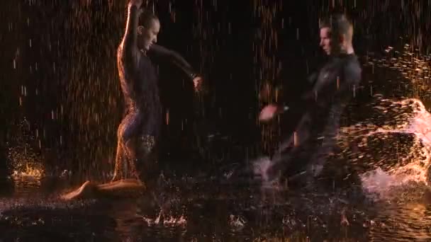 Динамічний і пристрасний джойстичний танець у виконанні професіоналів. Пара танцює під краплями дощу, рухаючись на поверхні води на чорному тлі підсвічування. Повільний рух. крупним планом . — стокове відео