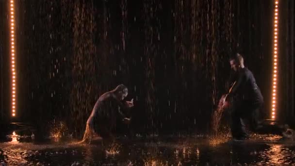 Страстная пара наслаждается выступлением веселого джайва под проливным дождем. Темная студия с постановочным желтым светом. Медленное движение. — стоковое видео