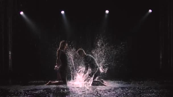 Profesjonalni tancerze towarzyscy wykonują jive elementy na ciemnym tle studio w deszczu. Zwolniony ruch. — Wideo stockowe