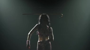 Genç Arap dansçı egzotik bir dansçı kafasında altın bir değnekle dans ediyor. Duman ve neon ışıkla karanlık bir stüdyoda çekildi. Siluetler. Kapat..