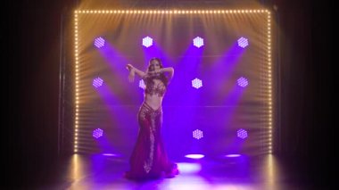 Geleneksel oryantal dansçı kız duman ve mavi neon ışıklı arka planda dans ediyor..