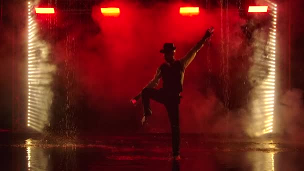 A man is silhouetted with glowing grenade in a dark smoky studio. A stylish entertainer performs a fire show in the rain against a backdrop of backlit red smoke. Slow motion. — Stock Video