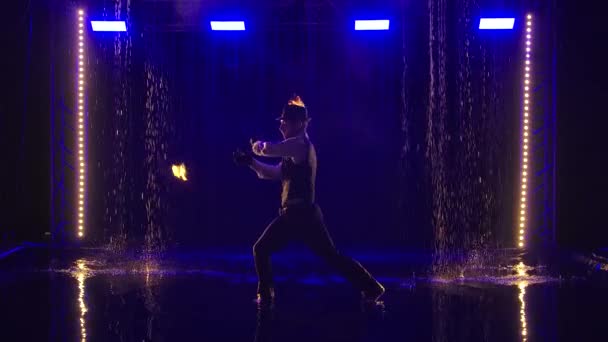 Een mannelijke artiest die 's nachts in slow motion een vuurshow opvoert. Fireshow in een donkere studio onder regendruppels. Silhouet. — Stockvideo