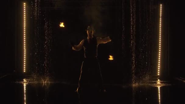 Захоплююче нічне вогняне шоу у виконанні стильного чоловіка, який виступає під дощем. Силует фейкіра на чорному тлі з студійним сценічним світлом. Повільний рух . — стокове відео