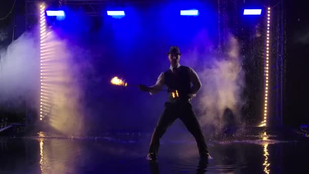 Tüzes előadás égő fáklyával, amit egy öltönyös és kalapos férfi ad elő. Tűzbemutató az esőben a stúdióban. Lassú mozgás.. — Stock videók