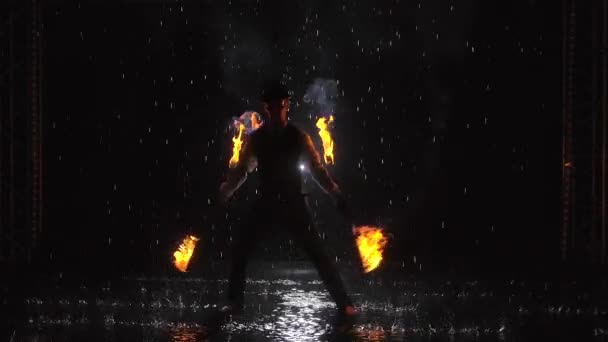 Silhouette of a man doing a professional fire show in a dark studio in the rain. Slow motion. — Stock Video