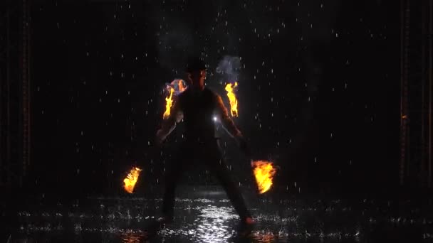 Silhouette of a man doing a professional fire show in a dark studio in the rain. Slow motion.