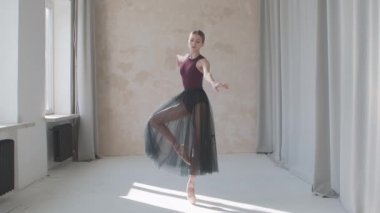 Kırılgan bir balerinin profesyonel performansı büyük panoramik pencere ve perdelerin arka planına karşı. Çatı katı tarzı bir stüdyoda çekildi. Gün ışığında yıkandı. Yavaş çekim.