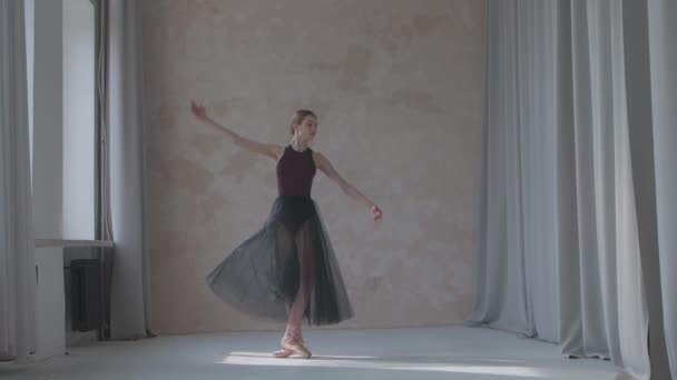 Bailarina con falda negra transparente hace ejercicios de ballet. Ensayos de danza se mueven por la ventana en el amplio estudio bañado por la luz del sol. Movimiento lento. — Vídeo de stock