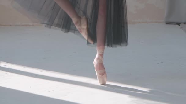 Bailarina en falda negra transparente muestra pases clásicos de ballet. Bailarinas de ballet pies mientras practica ejercicios puntiagudos en los pisos de parquet blanco. De cerca. Movimiento lento. — Vídeos de Stock