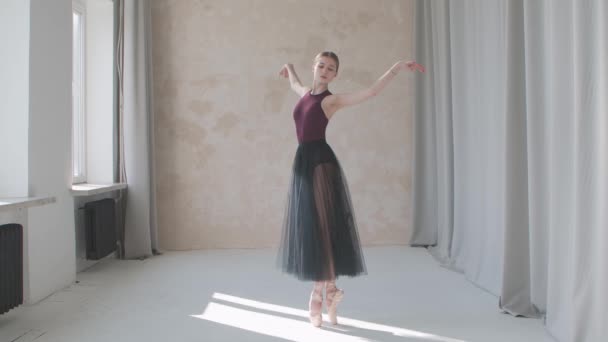 Professionelle Darstellung einer zerbrechlichen Ballerina vor dem Hintergrund großer Panoramafenster und Vorhänge. Gedreht wurde in einem Studio im Loft-Stil, das in helles Tageslicht getaucht ist. Zeitlupe. — Stockvideo