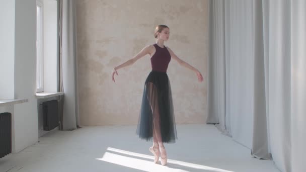 Professionell prestanda av en bräcklig ballerina mot bakgrund av stora panoramafönster och gardiner. Inspelad i en loft stil studio badade i starkt dagsljus. Långsamma rörelser. — Stockvideo