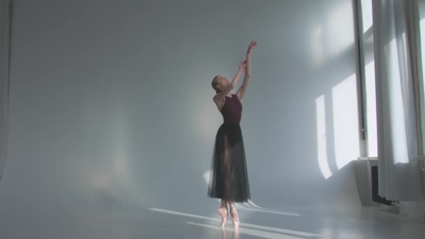 身着黑色芭蕾裙的芭蕾舞女芭蕾演员在靠近窗户的课堂上跳古典舞。表演前一个人热身明亮的日光下,一间宽敞的演播室的白色背景.慢动作. — 图库视频影像