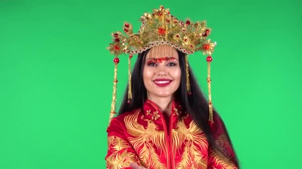 Güzel bir kadının portresi gülümsüyor ve jest yapıyor. Buraya gel. Kırmızı ipek kostüm ve Çinli bir prensesin başlığı içinde yanık esmer. Yeşil Ekran. — Stok video