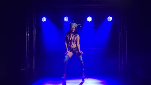 Mujer de piernas largas bailando en un estudio oscuro con humo y luces de neón azul. Atractiva morena en un traje sexy Estatua Americana de la Libertad y botas de tacón alto. Espectáculo de danza femenina erótica. Movimiento lento. — Vídeo de stock