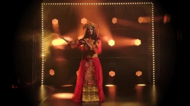 Kırmızı ipekli kadın dansçı ve Çinli prenseslerin başlığı. Çin halk dansları. Duman ve kırmızı neon ışıkla karanlık bir stüdyoda çekilmiş. Tiyatro dans gösterisi. Yavaş çekim