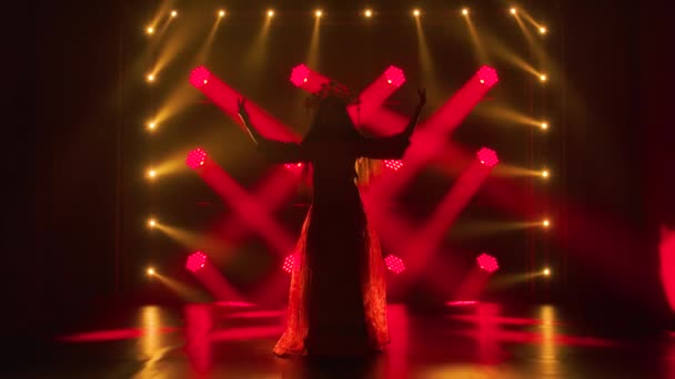 Jovem dançarina é silhueta em luzes vermelhas e fumaça realizando uma dança popular. Uma morena brilhante em um terno de seda vermelho e uma cobertura para a cabeça de uma princesa chinesa. Movimento lento. — Vídeo de Stock