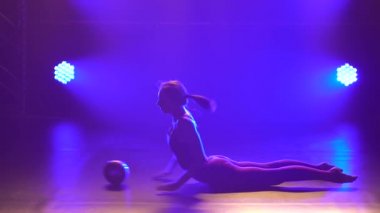 Sevimli jimnastikçi, topla ritmik jimnastik yapıyor. Karanlık bir stüdyoda neon ışıklı, bordo bir vücut giysisi giymiş bir kız..
