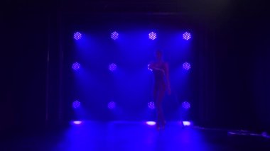 Burgundy vücudunda renkli kurdeleyle dans eden genç bir kız. Arka planda mavi ışıklar olan karanlık bir stüdyoda çekilmiş. İnce, esnek bir vücudun silueti. Yavaş çekim.