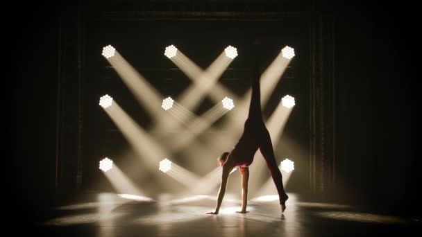 Chica deportiva gimnasta realiza ejercicios acrobáticos y estiramiento, mostrando la flexibilidad de su cuerpo. Grabado en un estudio oscuro con luces de neón. Silueta de un cuerpo delgado y flexible. Movimiento lento. — Vídeos de Stock