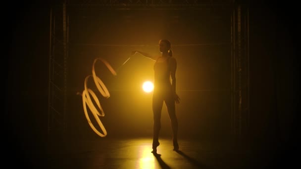 Štíhlá dívka sportovkyně v burgundských plavkách tančí se stuhou a protáhne se. Natočeno v tmavém ateliéru s krásným inscenovaným světlem. Silueta štíhlého pružného těla. Zpomalený pohyb. — Stock video