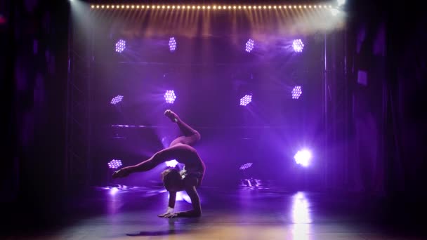 Chica gimnasta realiza ejercicios acrobáticos y estiramiento, mostrando la flexibilidad de su cuerpo. Grabado en un estudio oscuro con luces de neón. Silueta de un cuerpo delgado y flexible. Movimiento lento. — Vídeo de stock