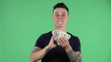 Yakışıklı bir gencin portresi kameraya bakıyor ve gururlu bir ifadeyle dolarları saçıyor, zengin hayatıyla övünüyor. Yeşil Ekran.