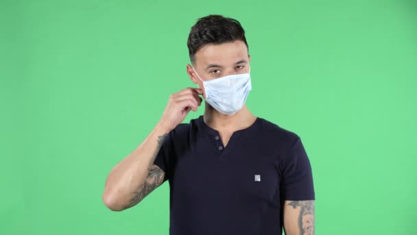 Portret van een knappe jongeman die naar de camera kijkt en een medisch beschermend masker verwijdert en lucht inademt. Gezondheidsbescherming Corona Virus Concept. Groen scherm. — Stockvideo