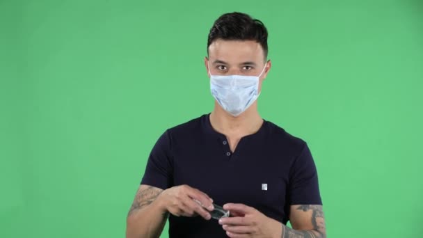 Πορτρέτο ενός όμορφου νεαρού άντρα σε ιατρική προστατευτική μάσκα προσώπου εφαρμόζει αντισηπτικό στα χέρια hir, προκειμένου να αποφευχθεί η εξάπλωση του coronavirus. Προστασία υγείας Corona Virus Concept. Πράσινη οθόνη — Αρχείο Βίντεο