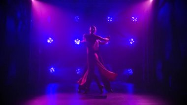 Yakışıklı adam ve kadın güzel ışığın arasında Latin dansı yapıyorlar. Yavaş çekimde dumanlı stüdyo arka planında dansçıların siluetleri.