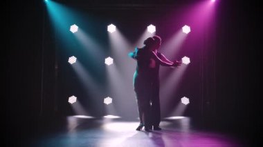 Duygusal ve sanatsal bir dans yapan şehvetli bir çiftin siluetleri. Ağır çekimde tangodan dans öğesi. Işıklı dumanlı stüdyo.