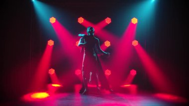 Profesyonel çift stüdyoda kırmızı ışıklarla tango yapıyor. Genç kadın ve erkek ağır çekimde Latince dans ediyorlar..