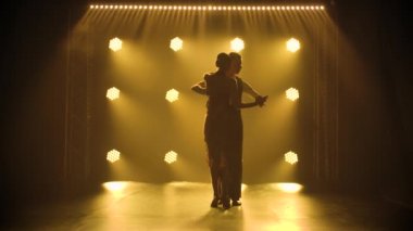 Aşık bir çift, stüdyoda sigara dumanı ve sarı ışık saçan tutkulu bir tango yapıyor. Ağır çekimde iki dansçının siluetleri.