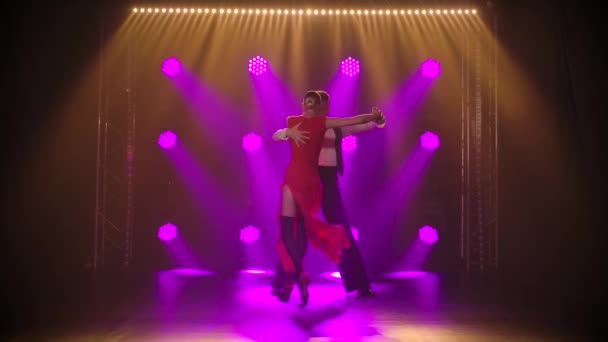 Namiętna młoda para w stylowych kostiumach tańcząca klasyczne argentyńskie tango w ciemnym studiu z neonowymi światłami. Zwolniony ruch. — Wideo stockowe