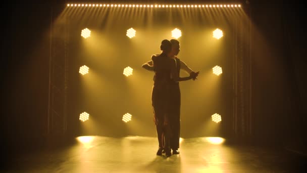 Couple in love dancing passionate tango in studio with smoke and yellow back light. Silhouettes of two dancers in slow motion. — Stock Video