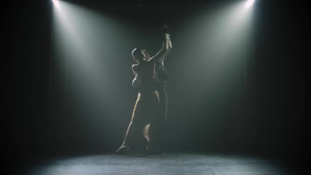 A young woman approaches her partner passionately and the couple dances Argentine tango. Dark silhouettes against the lights in the studio. Slow motion. — Stock Video