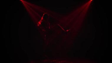 Genç bir kız tarafından gerçekleştirilen caz funk hareketleri. Stüdyonun arka planında çok renkli ışınlar içinde dans eden bir kadının silueti. Disko tarzı. Yavaş çekim.