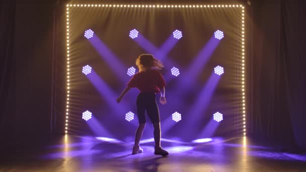 Genç kız stüdyoda ağır çekimde caz funk dansı yapıyor. Mavi ışıkların arkaplanına karşı siluet. — Stok video