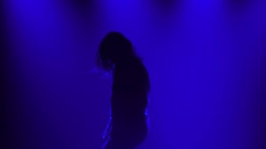 Stüdyoda dans eden genç kız modern koreografi Jazz funk. Mavi ışıklı dumanlı arka planda bir dansçının silüeti. Kapat..