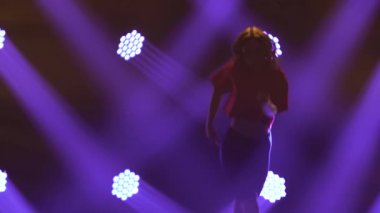 Genç bir kız dansçı tarafından yapılan modern funk caz hareketleri. Mor spot ışıklarının arka planında ince bir kızın silueti. Kapat..