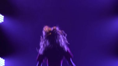 Aktif kız dansçı, koyu dumanlı bir stüdyoda arka plandaki mavi ışıklara karşı funky jazz yapıyor. Kapat..