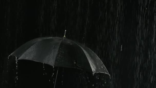 Um guarda-chuva preto aberto na chuva através do qual correm correntes de água. Filmado de perto em um estúdio escuro retroiluminado. Movimento lento. — Vídeo de Stock