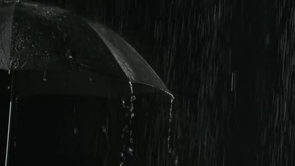 Regenstralen stromen door de open zwarte paraplu. Paraplu zonder iemand op een donkere studio achtergrond. Sluit maar af. Langzame beweging. — Stockvideo