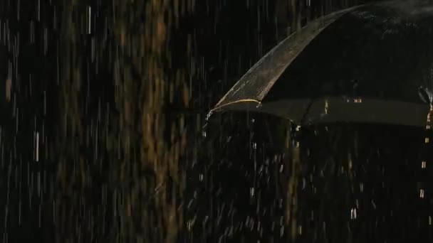 Gotas de lluvia con salpicaduras fluyen desde un paraguas negro abierto. Paraguas solitario en un fondo de estudio negro. De cerca. Movimiento lento. — Vídeos de Stock