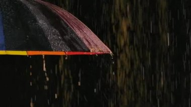 Şemsiyeye yağmur damlaları düşer ve stüdyo ışığında parlayan bir sürü sıçrama oluşur. Kapatın. Yavaş çekim.