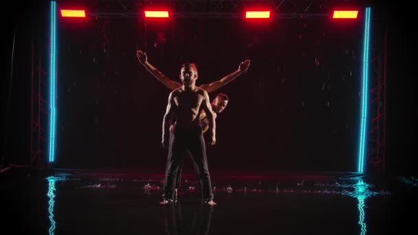 Un gruppo di uomini muscolosi con il busto nudo eseguono esercizi acrobatici. Girato in uno studio buio con luce rossa sulla superficie dell'acqua. Rallentatore. — Video Stock